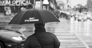 Ein Mann von hinten im Regen mit einem Regenschirm.