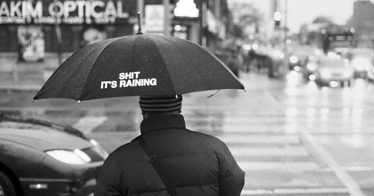 Ein Mann von hinten im Regen mit einem Regenschirm.
